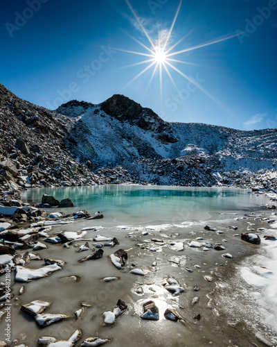 Türkisfarbener See auf der Macun Seenplatte im ersten Schnee im Herbst