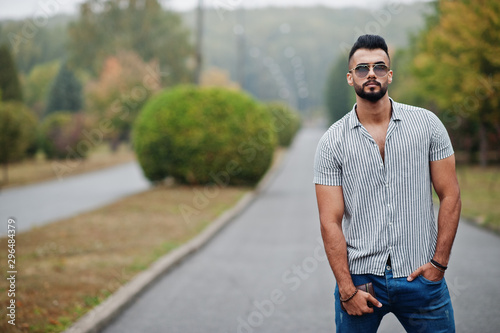 Fashionable tall arab beard man wear on shirt, jeans and sunglasses posed on park and hold wallet at hand.