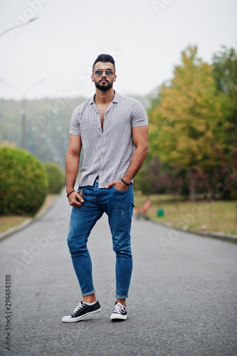 Fashionable tall arab beard man wear on shirt, jeans and sunglasses posed on park and hold wallet at hand.