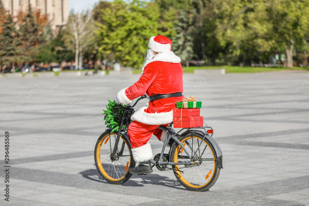 Santa Claus with Christmas gifts riding bicycle outdoors