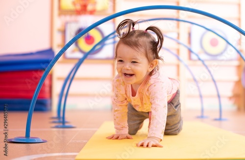 Baby toddler crawling on floor through tonnel in gym class. Lifestyle concept of children active games and exercises. photo