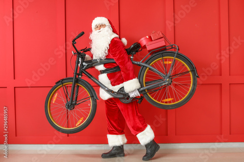 Santa Claus with Christmas gifts and bicycle on color background