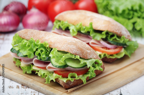 Two sandwiches with fresh vegetables, ham and cheese in ciabatta bread