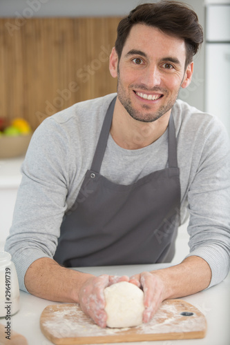 handsome man in apron smiling at camera while preparing pastry
