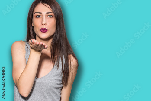 Happy young woman or teen girl in fancy dress and long hair sending blow kiss over vibrant blue background