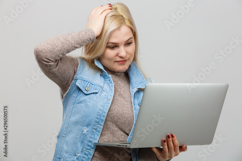 Young woman with laptop sitting on floor near light wall