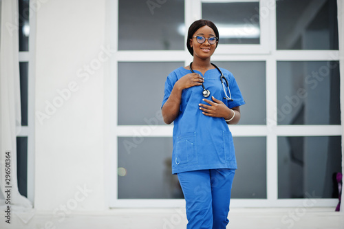 Portrait of happy female african american young doctor pediatrician in blue uniform coat and stethoscope against window in hospital. Healthcare, medical, medicine specialist - concept.