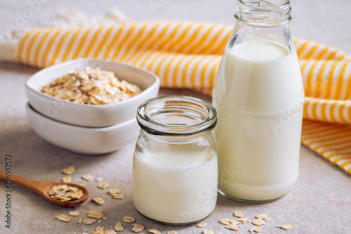 Bottle of oat milk and oat grains in bowl on table .