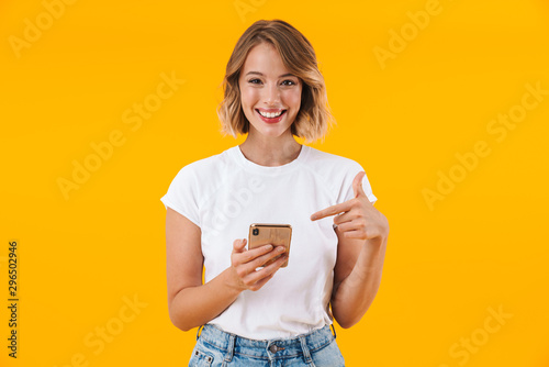 Image of joyful blond woman smiling and pointing finger at cellphone photo