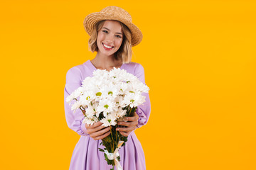 Image of content woman in elegant dress and straw hat holding flowers