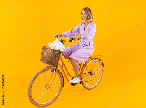 Fototapeta Naklejka Na Ścianę i Meble -  Full length image of woman in dress riding on bicycle with flowers