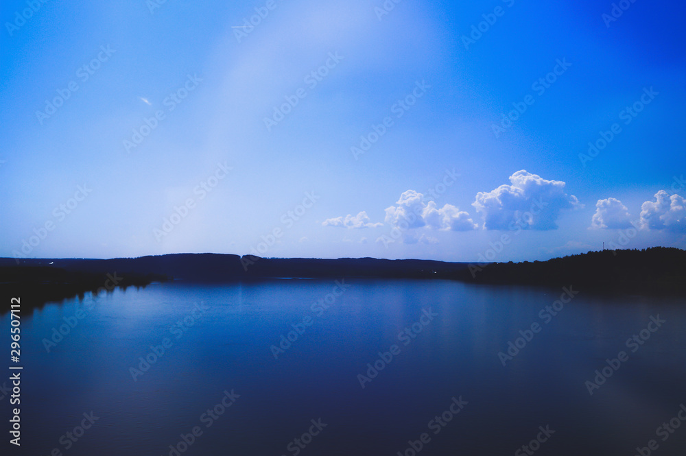 Fototapeta premium magical beauty river with a blue smooth surface. There is a clear sky above the water with one white cloud, and in the distance the earth and forests are visible. no unnecessary details, minimalistic 