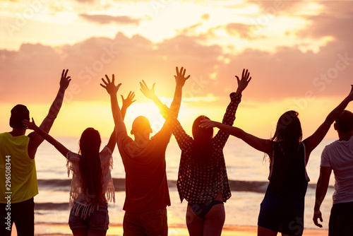Silhouettes of happy friends with raised arms against sunset sea