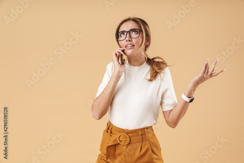 Image of puzzled young woman wearing eyeglasses talking on smartphone