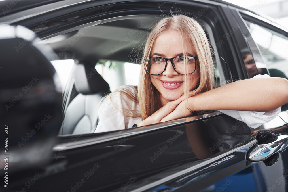 Nice reflection. Beautiful blonde girl sitting in the new car with modern black interior