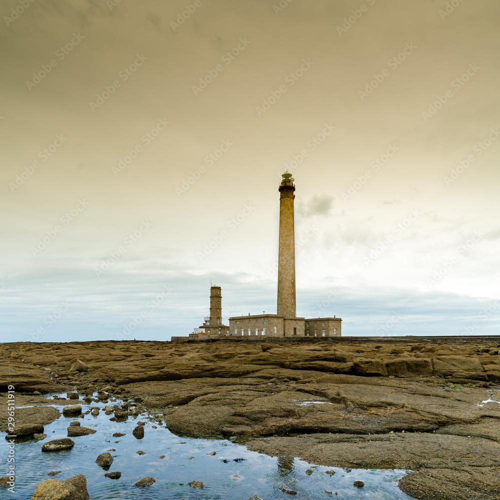 tall stone lighthouse with rocky shore tidal pools in foreground under a stormy sky