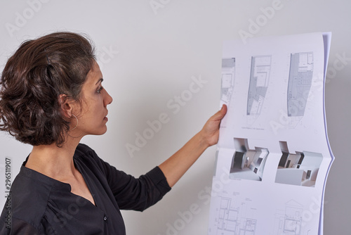  Young woman works as an architect in an office. She is brunette and Latina has a black shirt and different jobs on her table.