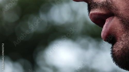 Young male with beard puffs on a vape pen device few drags outdoors, extreme close up photo