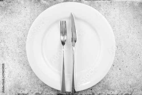 Table setting. Empty plate, knife and fork on a light concrete background. The fork and knife lie in parallel on a plate, the meal is over. Top view and flat lay with copy space.