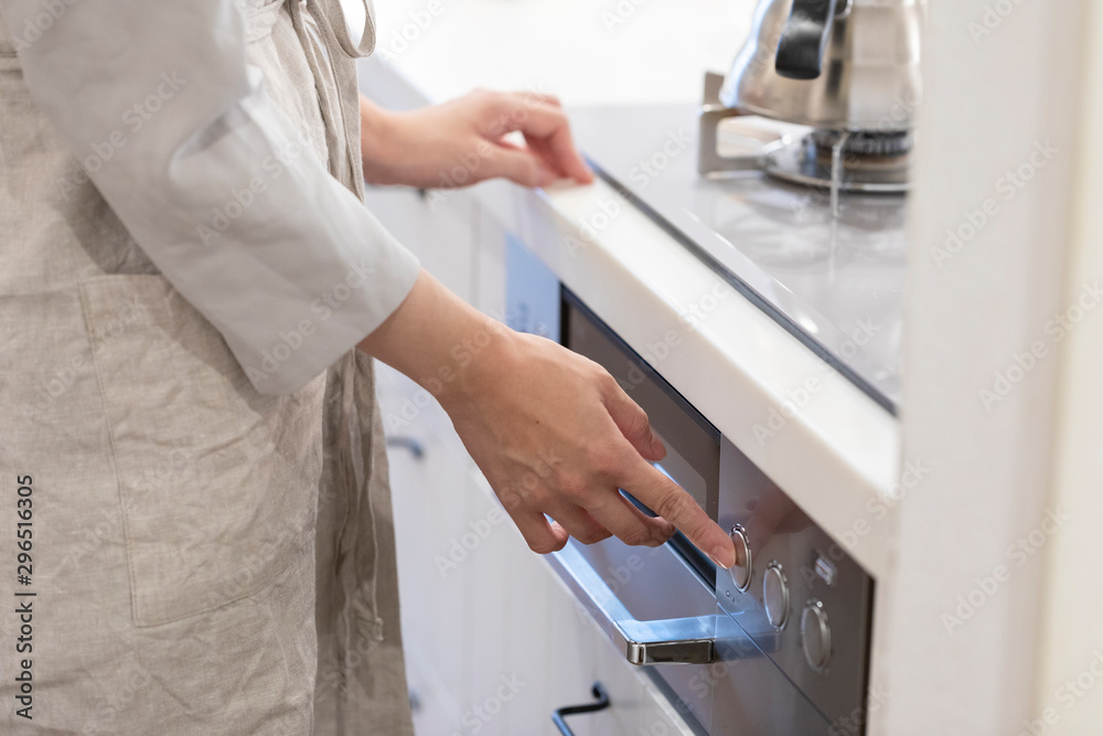 Obraz premium キッチンのガスコンロのボタンを押す若い女性の手元