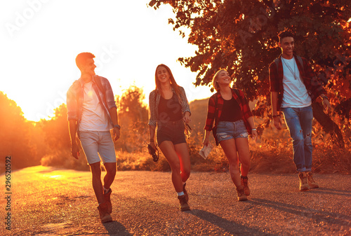 Group of four friends having fun hiking through countryside together on road during sunset.