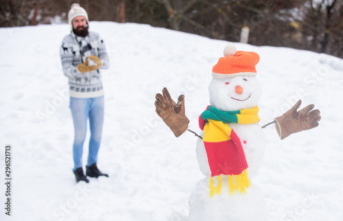 Snow games. Leisure on fresh air. Snowman and cheerful bearded hipster knitted hat and warm gloves play with snow outdoors. Have fun winter day. Let it snow. Christmas holidays. Active lifestyle