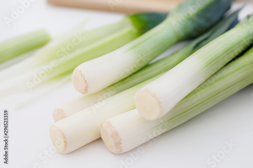 Bunch of fresh leeks in a white background with a wooden board and leeks pieces around it. Close up