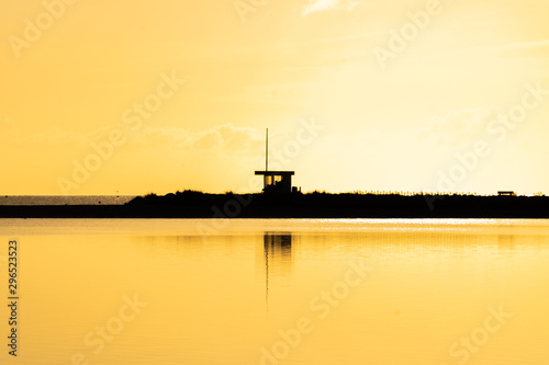 Golden hour on the ocean: The beach with a baywatch tower covered in golden light, the ocean reflecting the sunlight