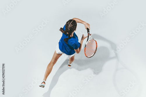 Young woman in blue shirt playing tennis. She hits the ball with a racket. Indoor studio shot isolated on white. Youth, flexibility, power and energy. Negative space. Top view. © master1305