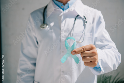 partial view of doctot in white coat holding blue awareness ribbon