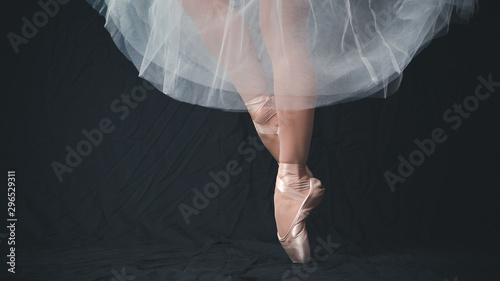 Close-up of dancing legs of ballerina wearing white pointe on a black background.