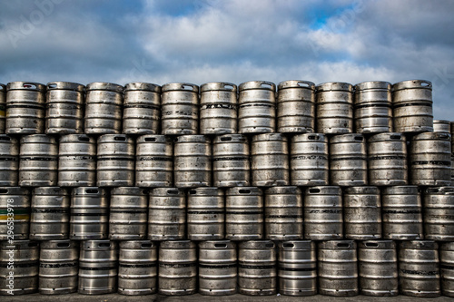 Pile of metal beer kegs stacked high outdoors, cloudy sky background