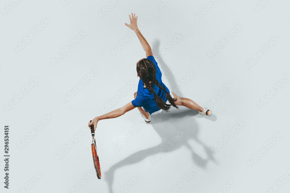 Naklejka premium Young woman in blue shirt playing tennis. She hits the ball with a racket. Indoor studio shot isolated on white. Youth, flexibility, power and energy. Negative space. Top view.