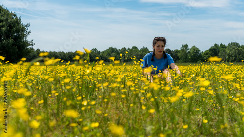 Teen girl sitting in large field with yellow flowers and trees in the background