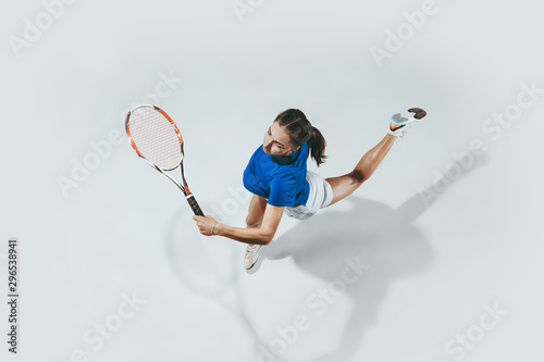 Young woman in blue shirt playing tennis. She hits the ball with a racket. Indoor studio shot isolated on white. Youth, flexibility, power and energy. Negative space. Top view. © master1305