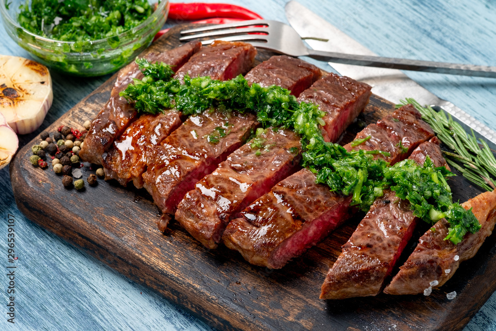 Sliced juicy beef steak with chimichurri sauce and spices on wooden board. Sliced juicy beef steak with chimichurri sauce and spices on wooden board.
