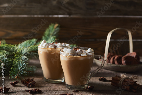 selective focus of cacao with marshmallow and cacao powder in mugs near pine branches, cinnamon and anise on wooden table