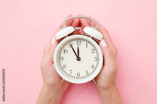 Woman hands holding white alarm clock on light pastel pink background. Time concept. Closeup. photo