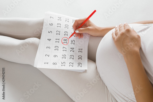 Young pregnant woman marking childbirth day in calendar. Baby expecting concept. Planning of future. photo