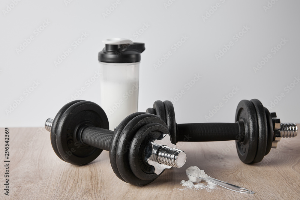 spoon with protein powder near dumbbells and sports bottle isolated on grey