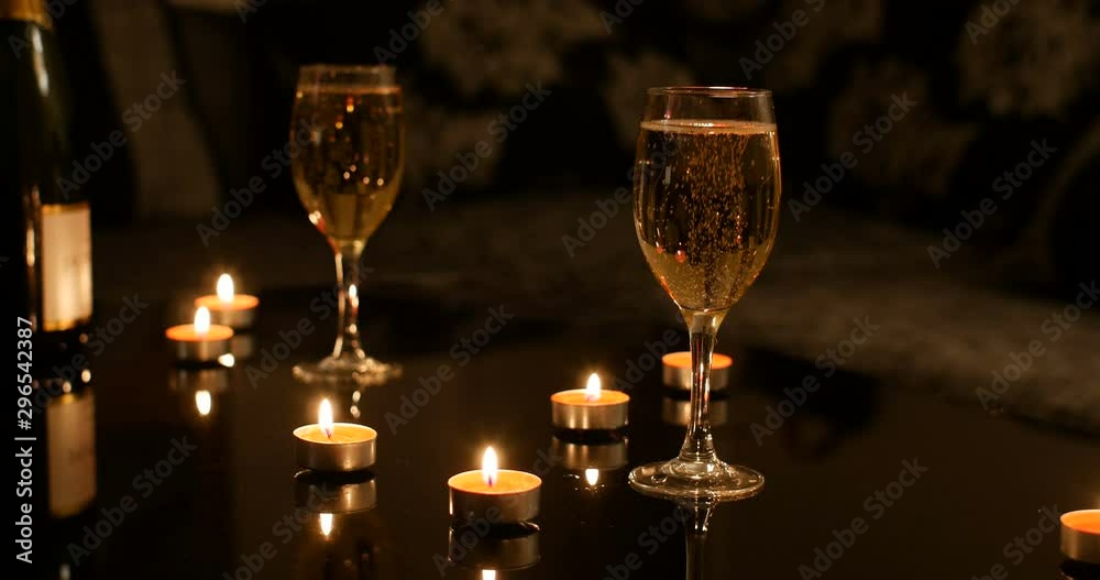 Glasses of champagne sparkling with nobody in background. On black glossy celebration table there is also red burning candles and bottle of sparkling wine. romantic valentine ambiance Glasses of champagne sparkling with nobody in background. On black glossy celebration table there is also red burning candles and bottle of sparkling wine. romantic valentine ambiance