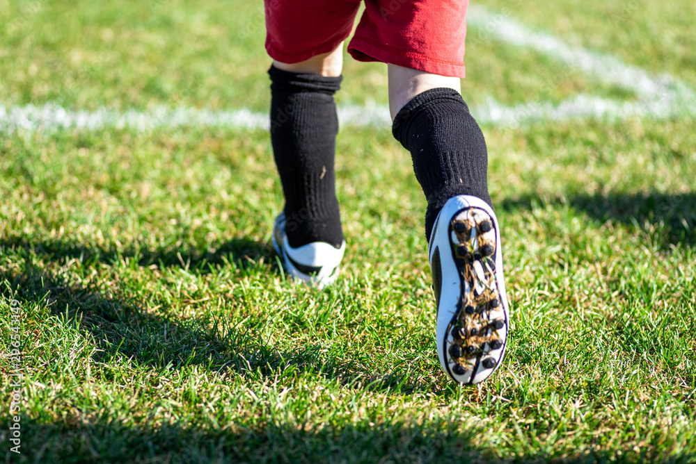 Fototapeta premium blurred for effect - action shot of young kid in cleats running onto soccer field