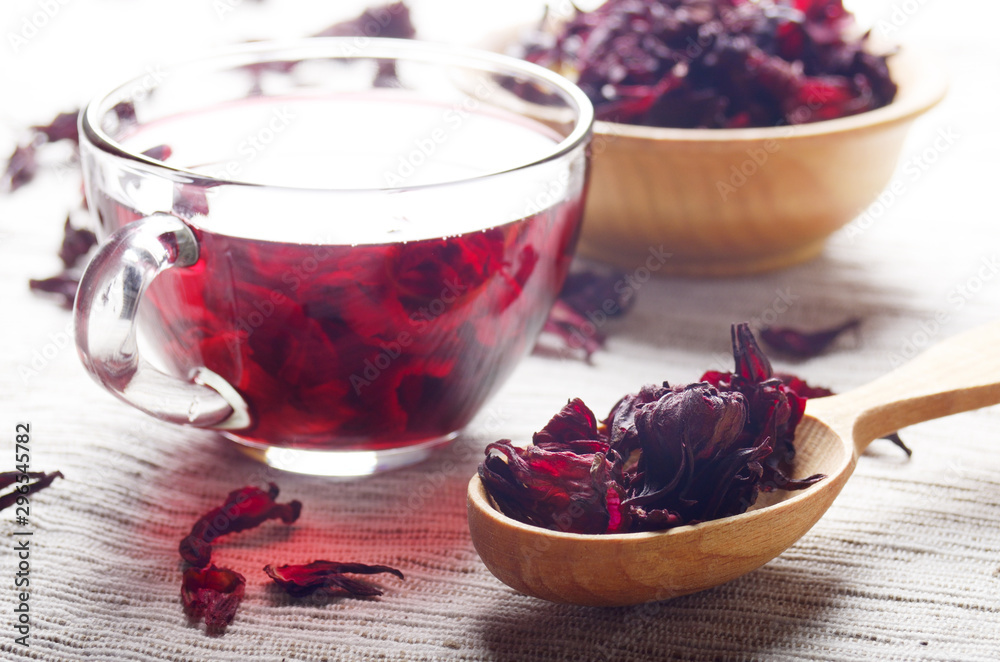 Closeup view at wooden bowl tea cup and spoon of dry hibiscus petals on linen cloth background Closeup view at wooden bowl tea cup and spoon of dry hibiscus petals on linen cloth background
