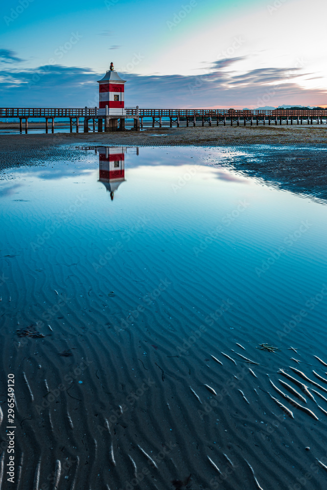Naklejka premium Sunrise over the sea. The lighthouse of Lignano Sabbiadoro and the games of sand and colors. Italy