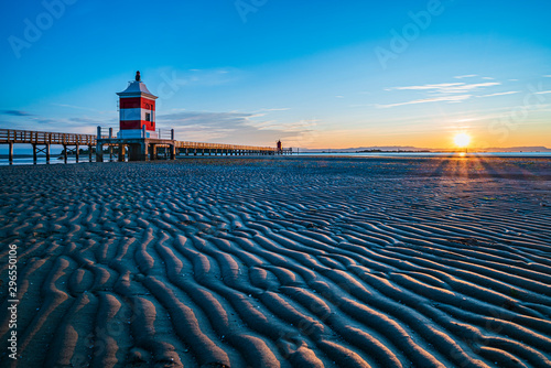 Sunrise over the sea. The lighthouse of Lignano Sabbiadoro and the games of sand and colors. Italy