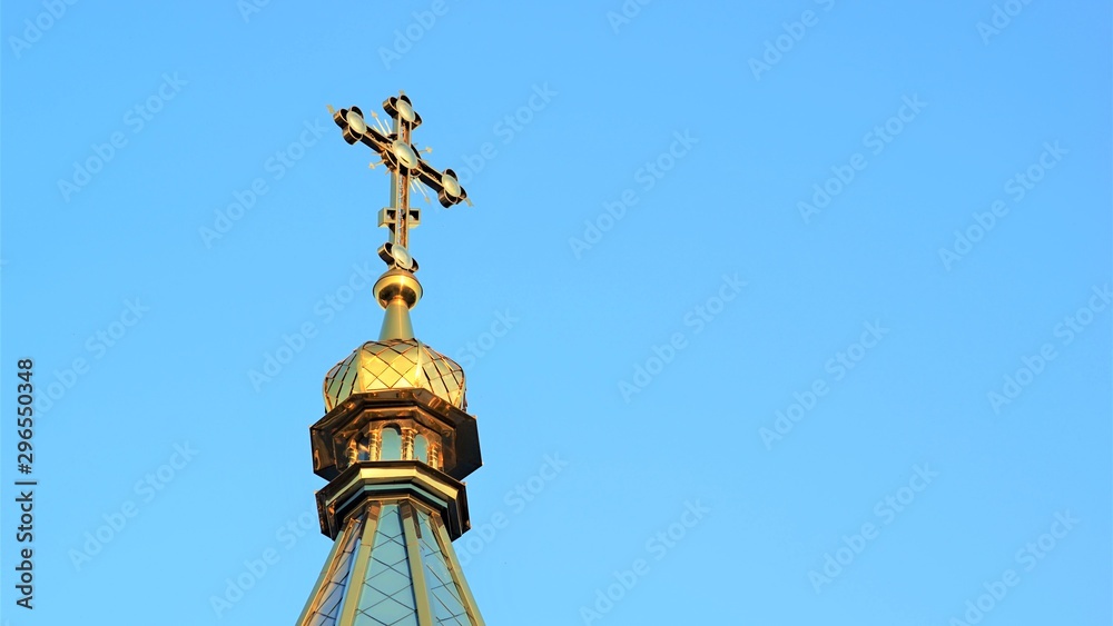 Roof top of the Orthodox Church with a cross against a blue sky.