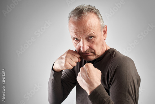 Elderly stylish man in boxing pose with strong face holds blow of fate, fights with life difficulties and problems on white studio background