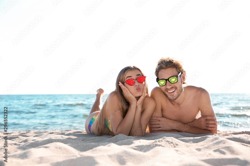 Fototapeta premium Happy young couple in sunglasses lying together on beach