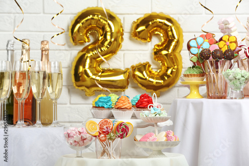 Dessert table in room decorated with golden balloons for 23 year birthday party