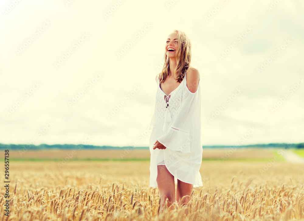 country, nature, summer holidays, vacation and people concept - smiling young woman in white dress on cereal field - obrazy, fototapety, plakaty 